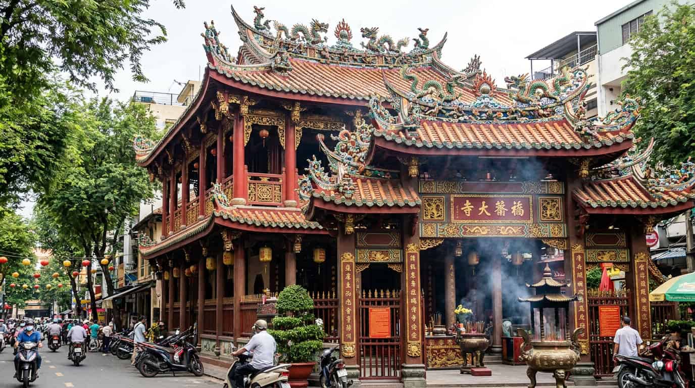 An ornate Cantonese-style pagoda in Cholon, Saigon, with elaborate ceramic roof decorations, red and gold color scheme, and incense smoke drifting from the entrance