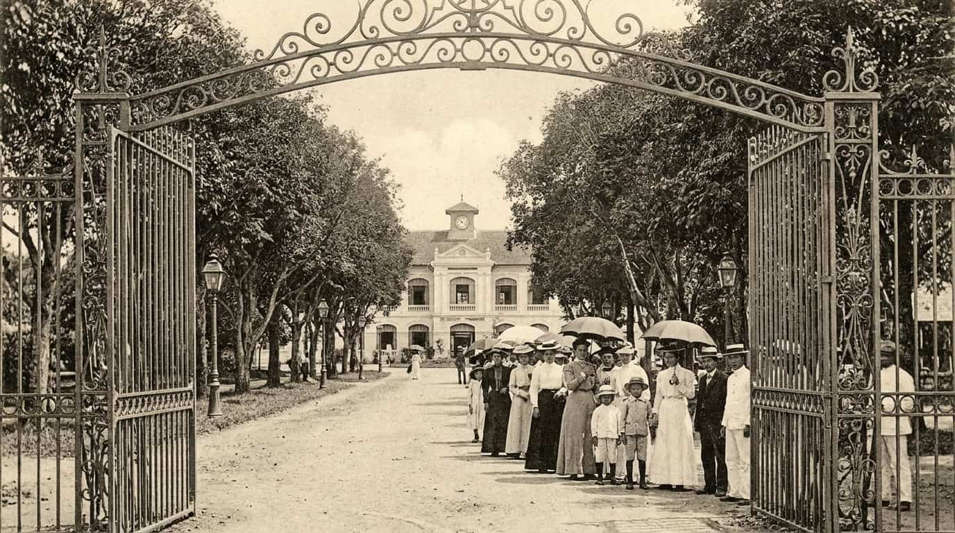 The historic entrance gate of the Saigon Zoo in Ho Chi Minh City, with its ornamental iron and stonework, seen from the main entrance road with tropical trees on either side.